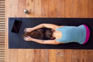 Overhead View Of Woman Stretching On Exercise Mat Using Digital Tablet