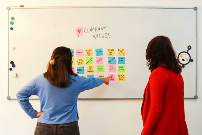 Two women standing in front of a whiteboard with sticky notes on it
