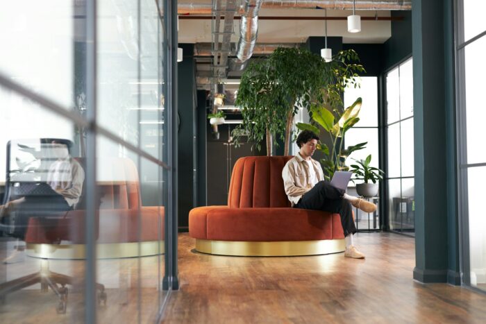 Young man with laptop in seating area of open plan office renting work space for start up business