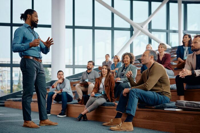 Black businessman talking to large group of entrepreneurs during education event in conference hall.