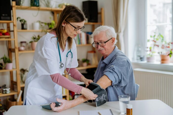 Female doctor visiting senior man and examinig him indoors at home.