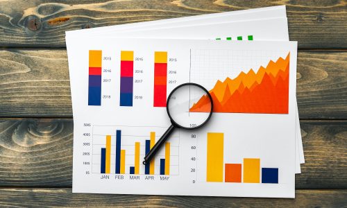 Business graphs and magnifying glass on table Business graphs and magnifying glass on table