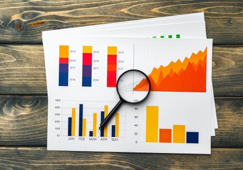 Business graphs and magnifying glass on table Business graphs and magnifying glass on table